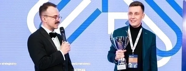 Dwóch mężczyzn stojących odpowiednio z mikrofonem oraz pucharem