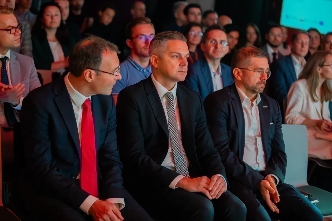 Trzech mężczyzn w garniturach siedzących wśród publiczości